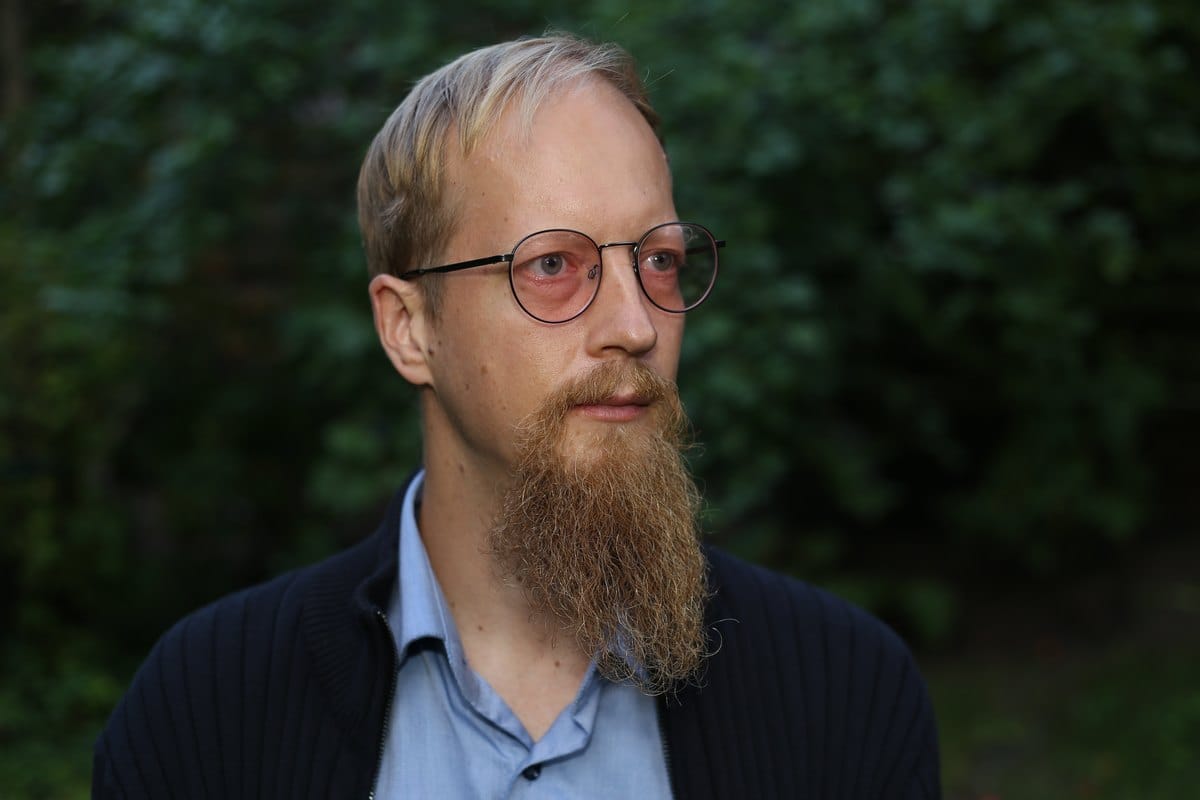 Juuso Kangas pyöreät silmälasit päässä, taustalla vihreää lehvästöä.
