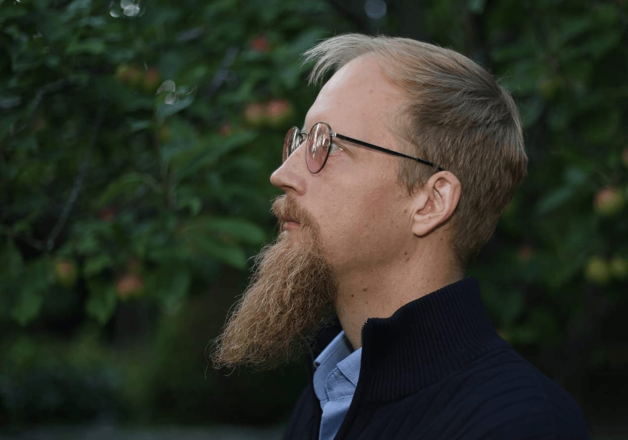 Juuso Kangas sivuprofiilissa silmälasit päässä, taustalla vihreää puutarhaa.